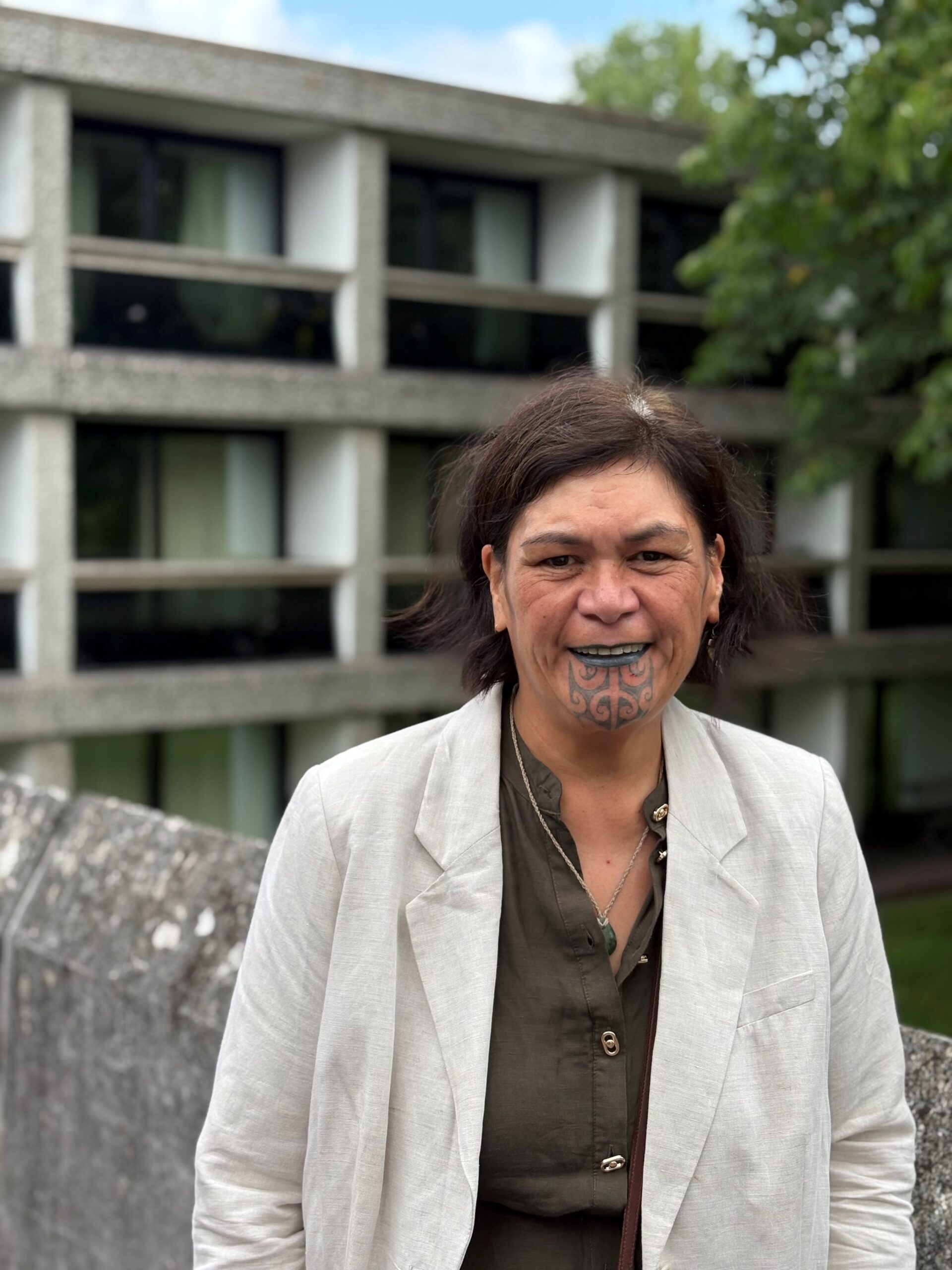 A lady with Maori moko or face tattoo stands in front of buildings at Wolfson College, Oxford