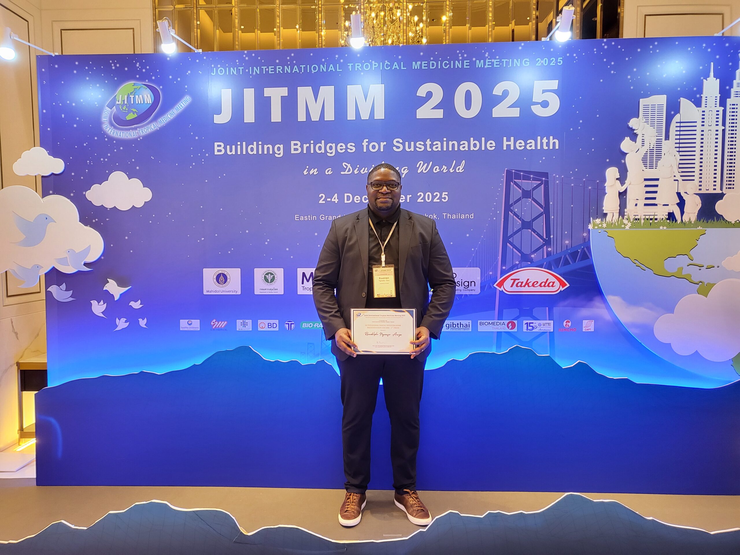 Oxford DPhil student Randolph Ngwafor stands in front of a poster advertising the Joint International Tropical Medicine Meeting in Bangkok, Thailand