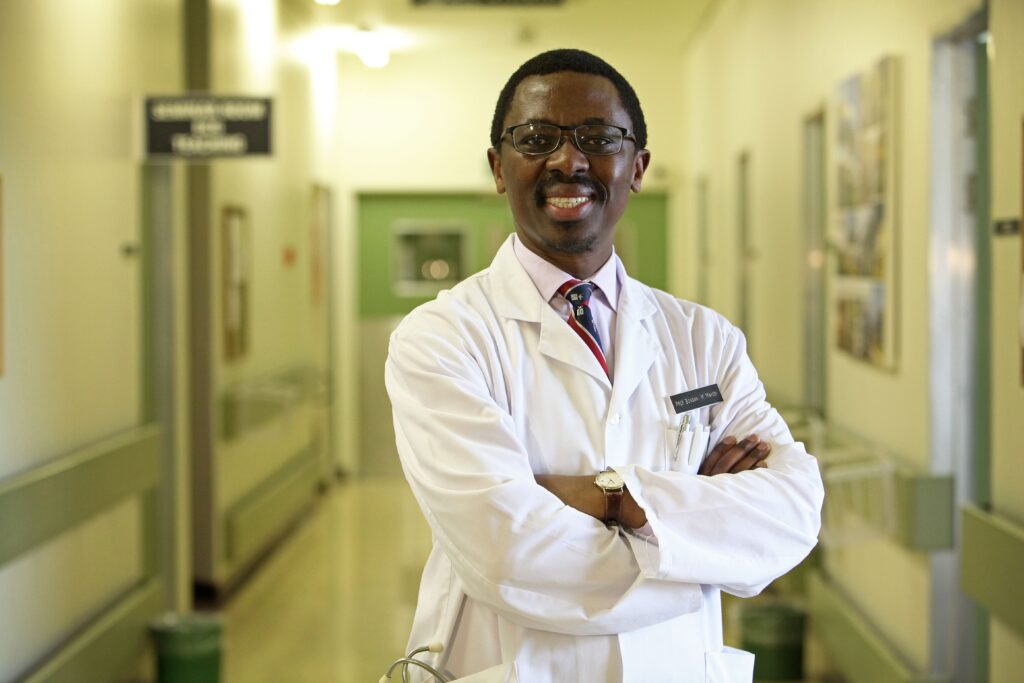 A smiling Bongani Mayosi stands in a hospital corridor in his white doctor's coat.